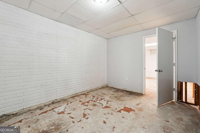 spare room with concrete floors, brick wall, and a paneled ceiling