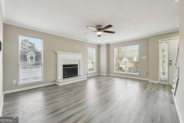 unfurnished living room featuring light hardwood / wood-style floors, a textured ceiling, ornamental molding, and a tiled fireplace