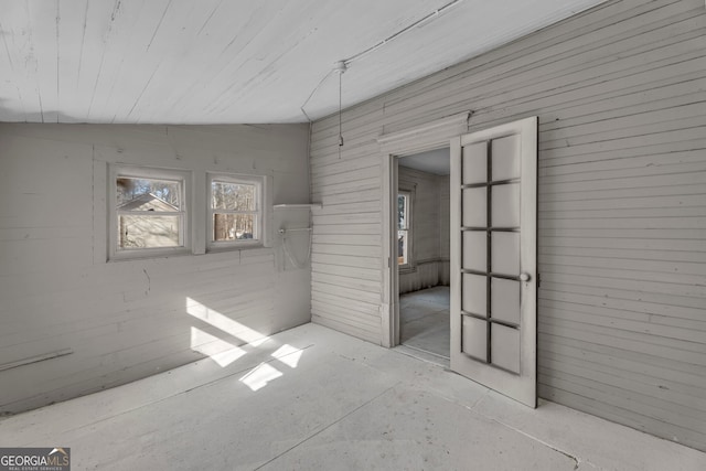 unfurnished room featuring lofted ceiling and wood walls