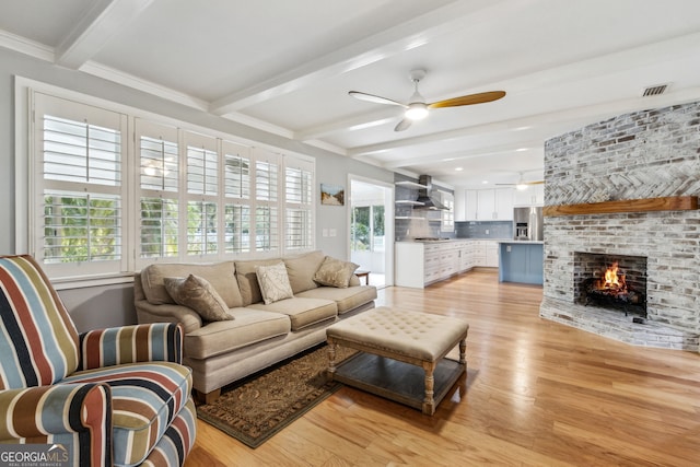 living room featuring crown molding, ceiling fan, beam ceiling, a fireplace, and light wood-type flooring