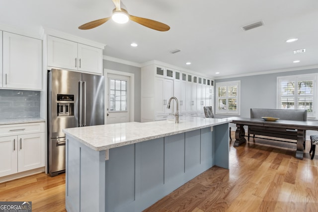 kitchen with white cabinetry, high end refrigerator, a kitchen island with sink, light stone countertops, and light hardwood / wood-style flooring