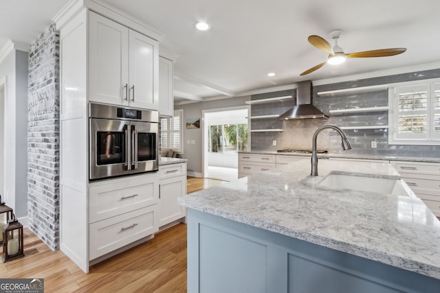 kitchen with appliances with stainless steel finishes, wall chimney exhaust hood, sink, and white cabinets