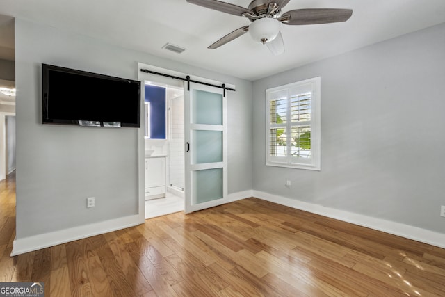 unfurnished bedroom featuring ceiling fan, a barn door, connected bathroom, and light hardwood / wood-style floors