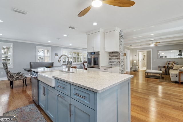 kitchen featuring an island with sink, sink, white cabinets, stainless steel appliances, and light hardwood / wood-style flooring