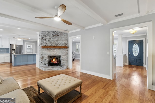 living room with beamed ceiling, ornamental molding, a fireplace, and light hardwood / wood-style flooring