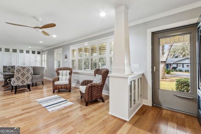 living area with crown molding, light wood-type flooring, a wealth of natural light, and ornate columns