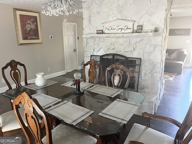 dining room featuring wood-type flooring, a stone fireplace, and a notable chandelier