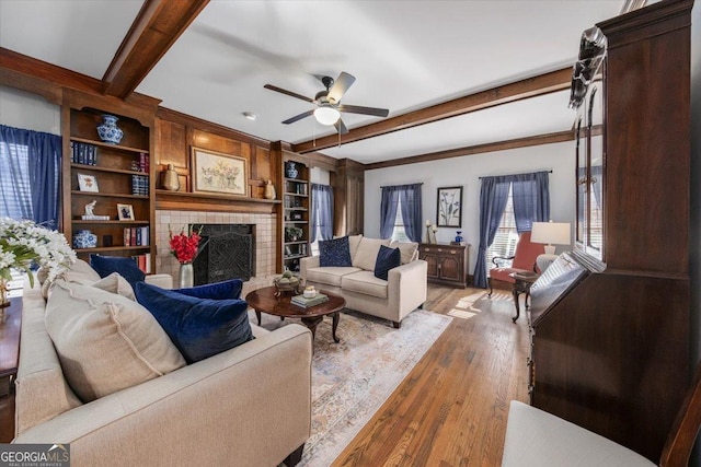 living room featuring light hardwood / wood-style floors, built in features, ceiling fan, beam ceiling, and a tiled fireplace