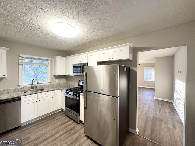 kitchen featuring sink, light stone counters, stainless steel appliances, and white cabinetry