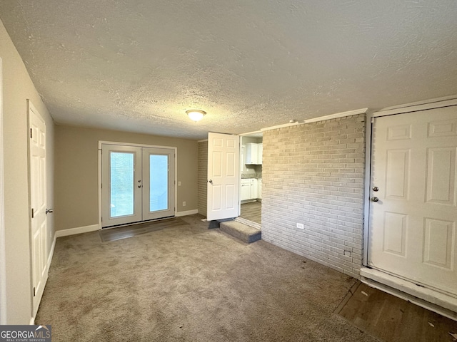 interior space with french doors, brick wall, a textured ceiling, and carpet flooring