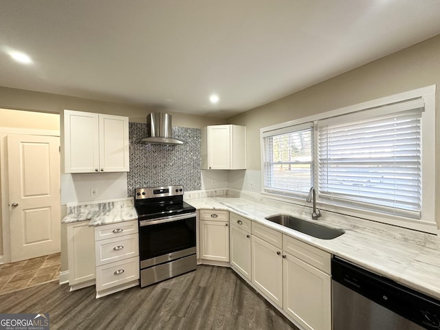 kitchen with appliances with stainless steel finishes, white cabinets, dark wood-type flooring, wall chimney range hood, and sink