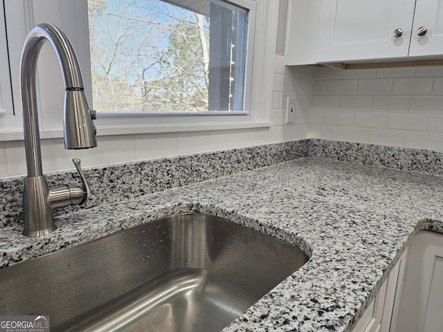 room details featuring light stone counters, sink, white cabinetry, and backsplash