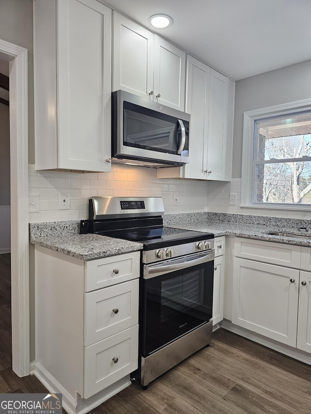 kitchen with white cabinets, dark wood-type flooring, stainless steel appliances, decorative backsplash, and light stone counters