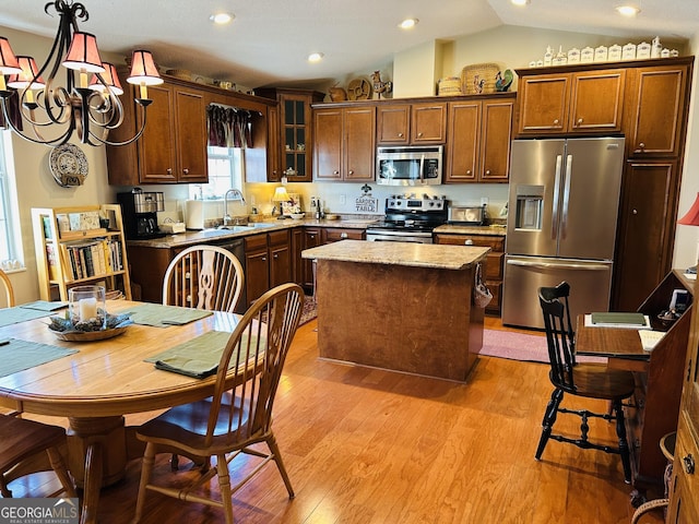 kitchen with vaulted ceiling, a kitchen island, stainless steel appliances, sink, and light wood-type flooring