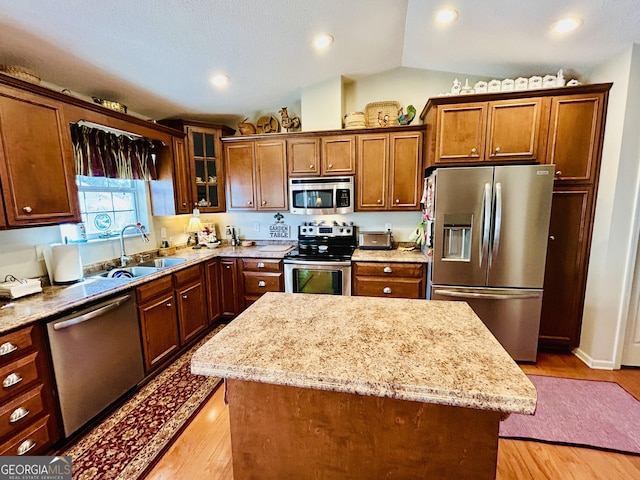 kitchen with lofted ceiling, a center island, sink, light stone countertops, and stainless steel appliances