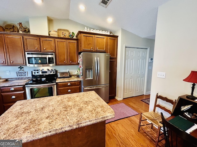 kitchen featuring light hardwood / wood-style floors, stainless steel appliances, lofted ceiling, light stone counters, and a center island