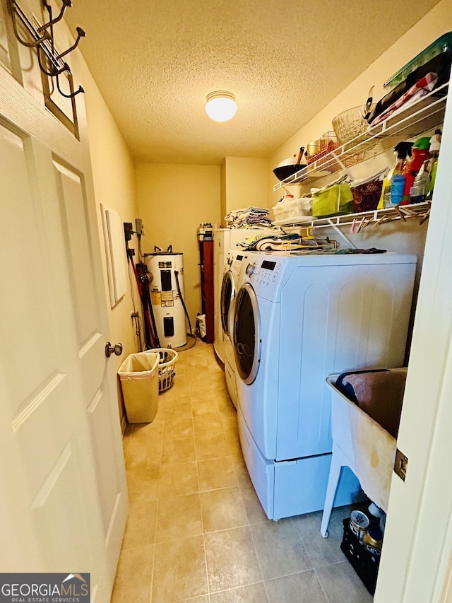 washroom with water heater, a textured ceiling, light tile patterned floors, and independent washer and dryer