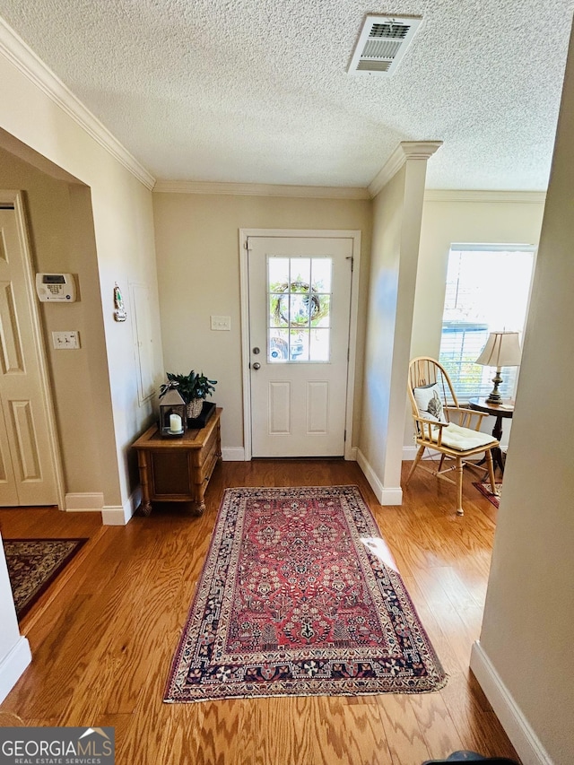 entryway with a textured ceiling, decorative columns, ornamental molding, and hardwood / wood-style floors