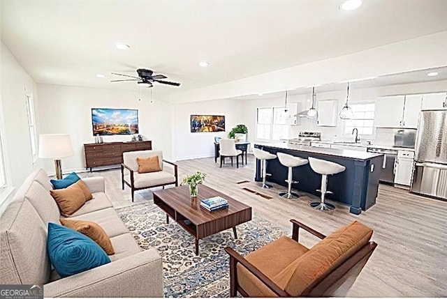 living room featuring ceiling fan, sink, and light hardwood / wood-style flooring