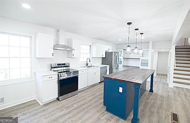 kitchen featuring a kitchen island, hanging light fixtures, wall chimney exhaust hood, stainless steel appliances, and butcher block counters