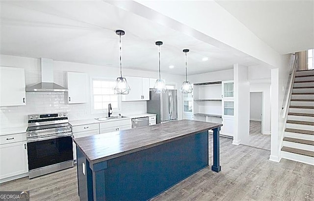 kitchen featuring stainless steel appliances, wall chimney range hood, a kitchen island, white cabinets, and sink