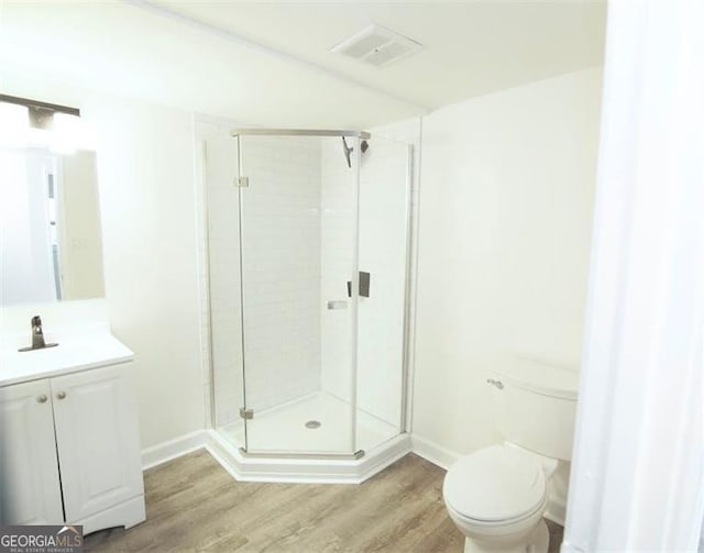 bathroom with toilet, hardwood / wood-style flooring, a shower with door, and vanity