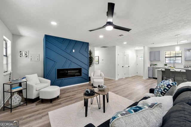 living room featuring ceiling fan, a textured ceiling, light hardwood / wood-style flooring, and a fireplace