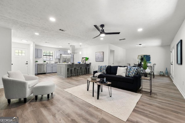 living room featuring ceiling fan, a textured ceiling, and light wood-type flooring