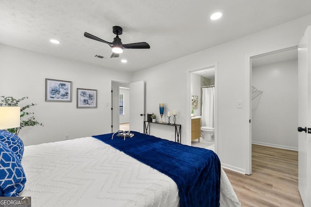 bedroom featuring ensuite bath, ceiling fan, light wood-type flooring, and a textured ceiling