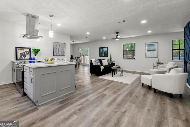 kitchen featuring pendant lighting, a textured ceiling, island range hood, stainless steel electric range oven, and light wood-type flooring