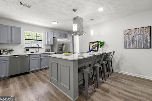 kitchen featuring gray cabinetry, appliances with stainless steel finishes, pendant lighting, and island range hood