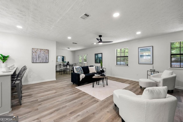 living room featuring light hardwood / wood-style floors, a textured ceiling, and ceiling fan