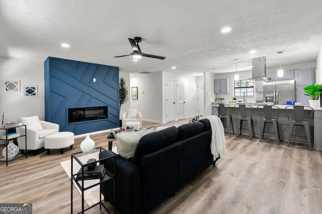 living room featuring ceiling fan, a textured ceiling, and light wood-type flooring