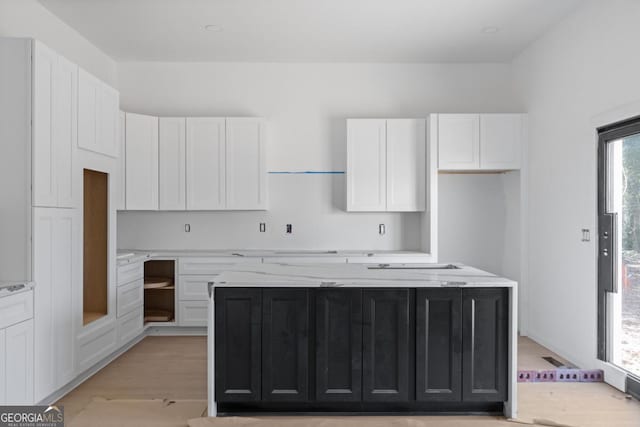 kitchen featuring light wood-type flooring, white cabinetry, light stone counters, and a kitchen island