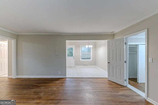 empty room featuring an inviting chandelier, ornamental molding, and wood-type flooring