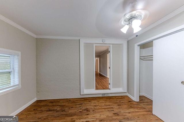 unfurnished bedroom featuring ceiling fan, hardwood / wood-style floors, ornamental molding, a closet, and brick wall