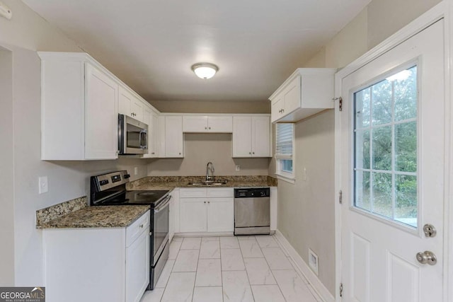 kitchen with stainless steel appliances, white cabinetry, dark stone counters, and sink