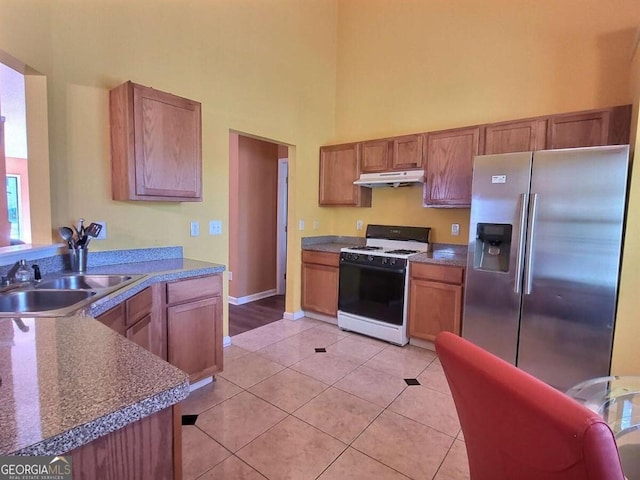 kitchen featuring gas range gas stove, a towering ceiling, stainless steel refrigerator with ice dispenser, sink, and light tile patterned floors