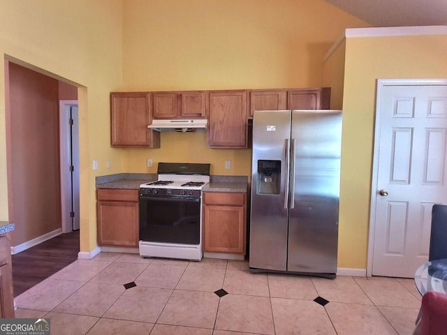 kitchen with light tile patterned floors, stainless steel fridge with ice dispenser, and white gas range