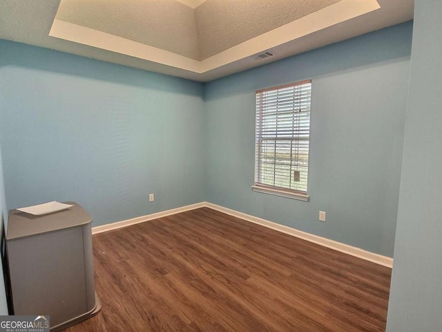 spare room with dark wood-type flooring and a tray ceiling