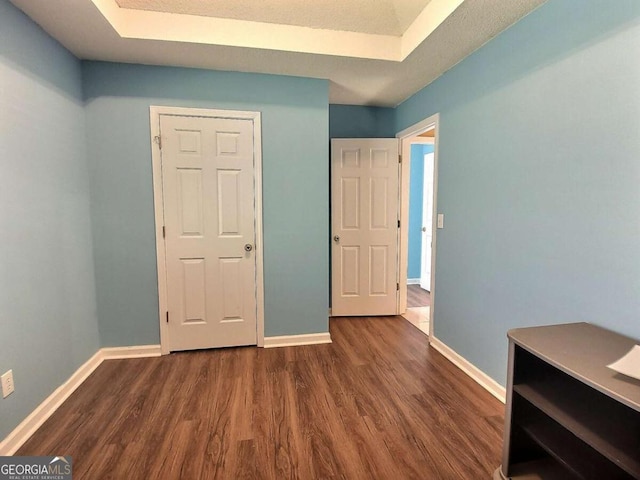 unfurnished bedroom with a raised ceiling and dark wood-type flooring