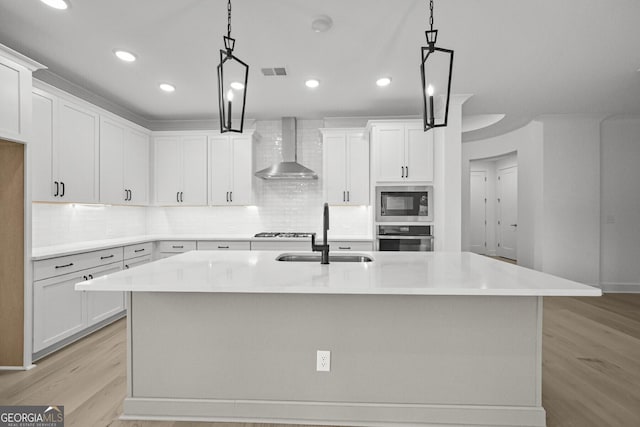 kitchen featuring wall chimney exhaust hood, a sink, appliances with stainless steel finishes, light wood-type flooring, and decorative backsplash