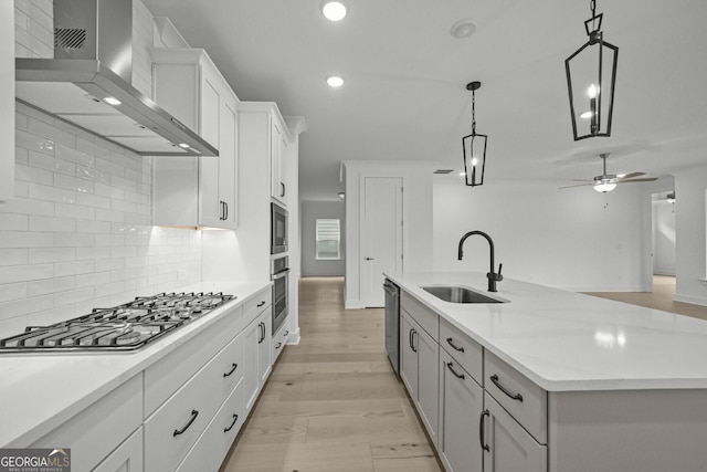 kitchen with a sink, wall chimney range hood, stainless steel appliances, tasteful backsplash, and a center island with sink