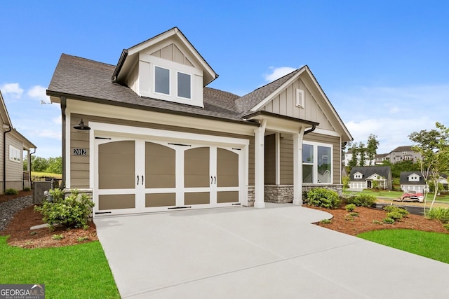 craftsman-style house featuring board and batten siding, driveway, stone siding, and a shingled roof