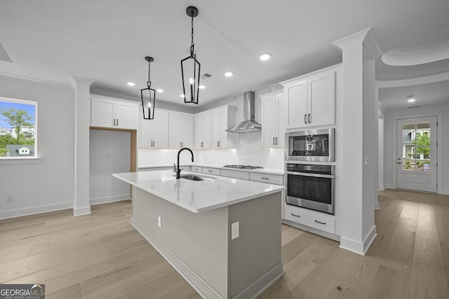 kitchen featuring stainless steel appliances, a sink, wall chimney range hood, light wood-style flooring, and recessed lighting
