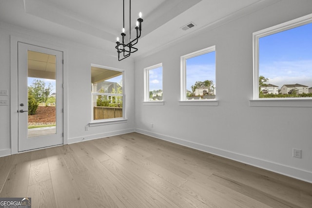 unfurnished dining area with wood finished floors, a chandelier, plenty of natural light, and baseboards