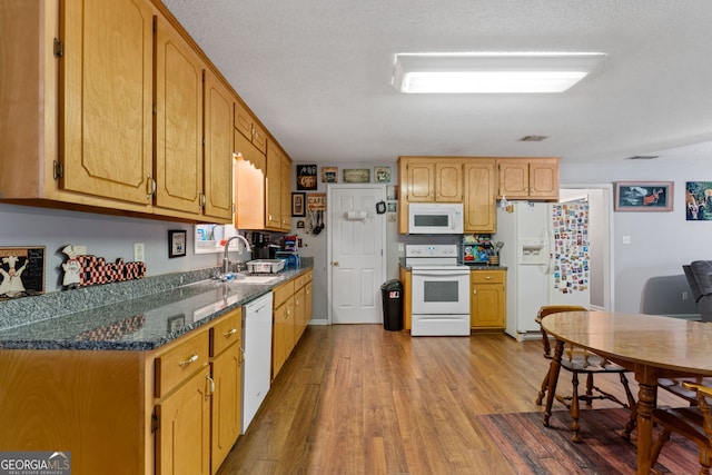 kitchen with white appliances, dark stone countertops, a textured ceiling, light hardwood / wood-style flooring, and sink