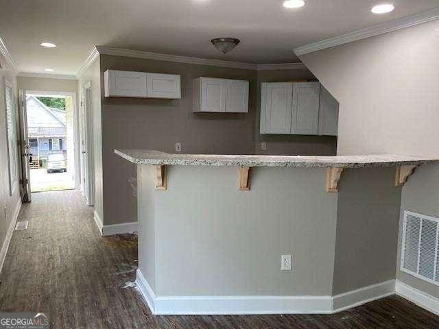 kitchen featuring white cabinets, dark wood-type flooring, a breakfast bar area, and ornamental molding