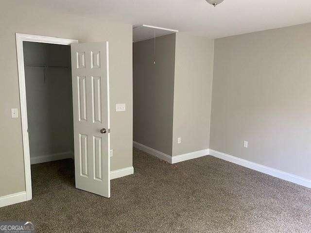 unfurnished bedroom featuring a closet, a spacious closet, and dark carpet