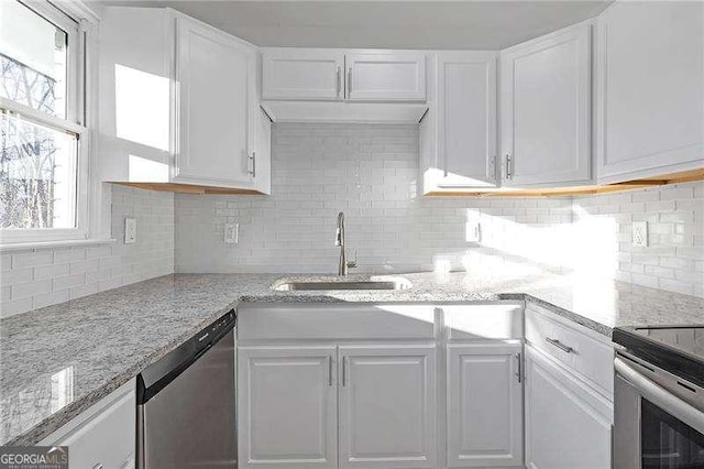 kitchen featuring light stone countertops, appliances with stainless steel finishes, white cabinetry, decorative backsplash, and sink